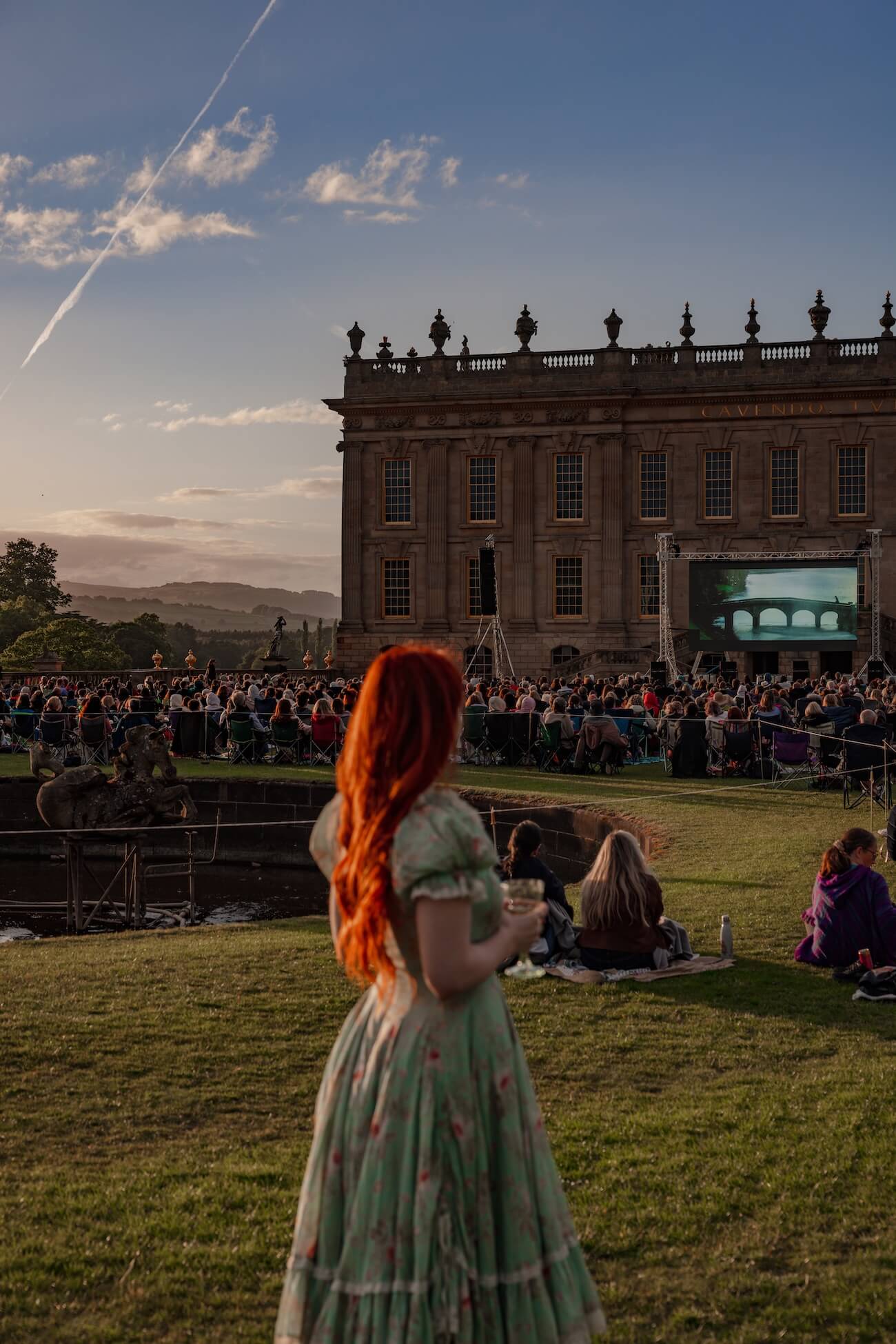 Woman with red hair standing at Chatsworth House lawn in front of an outdoor cinema showing Pride and Prejudice